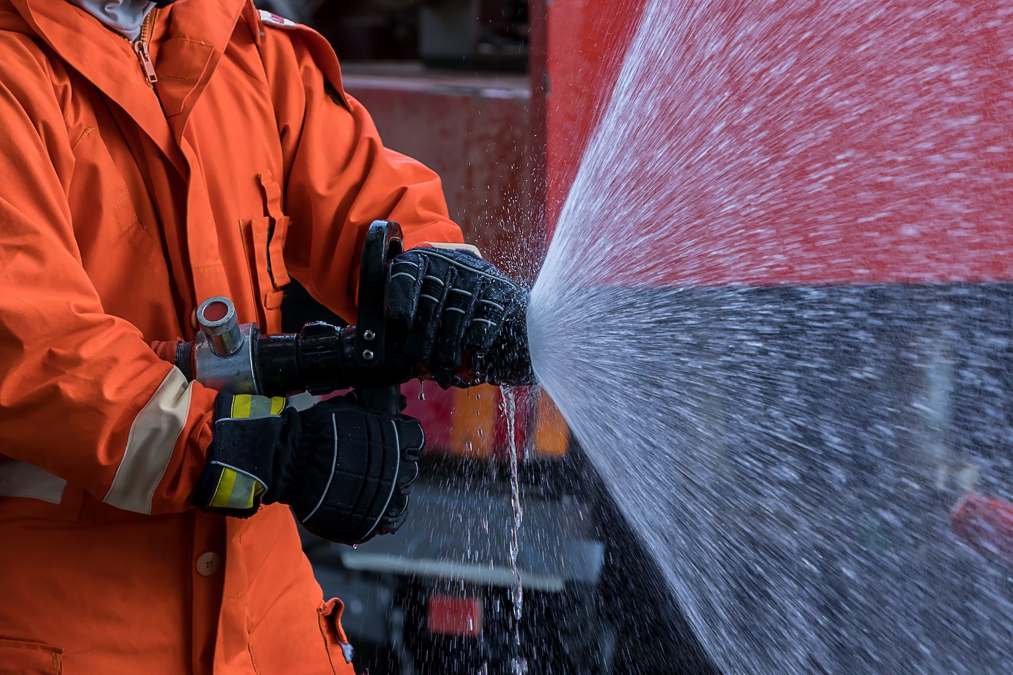Fire man spray water from hose for fire fighting. Firefighter spraying a straight steam