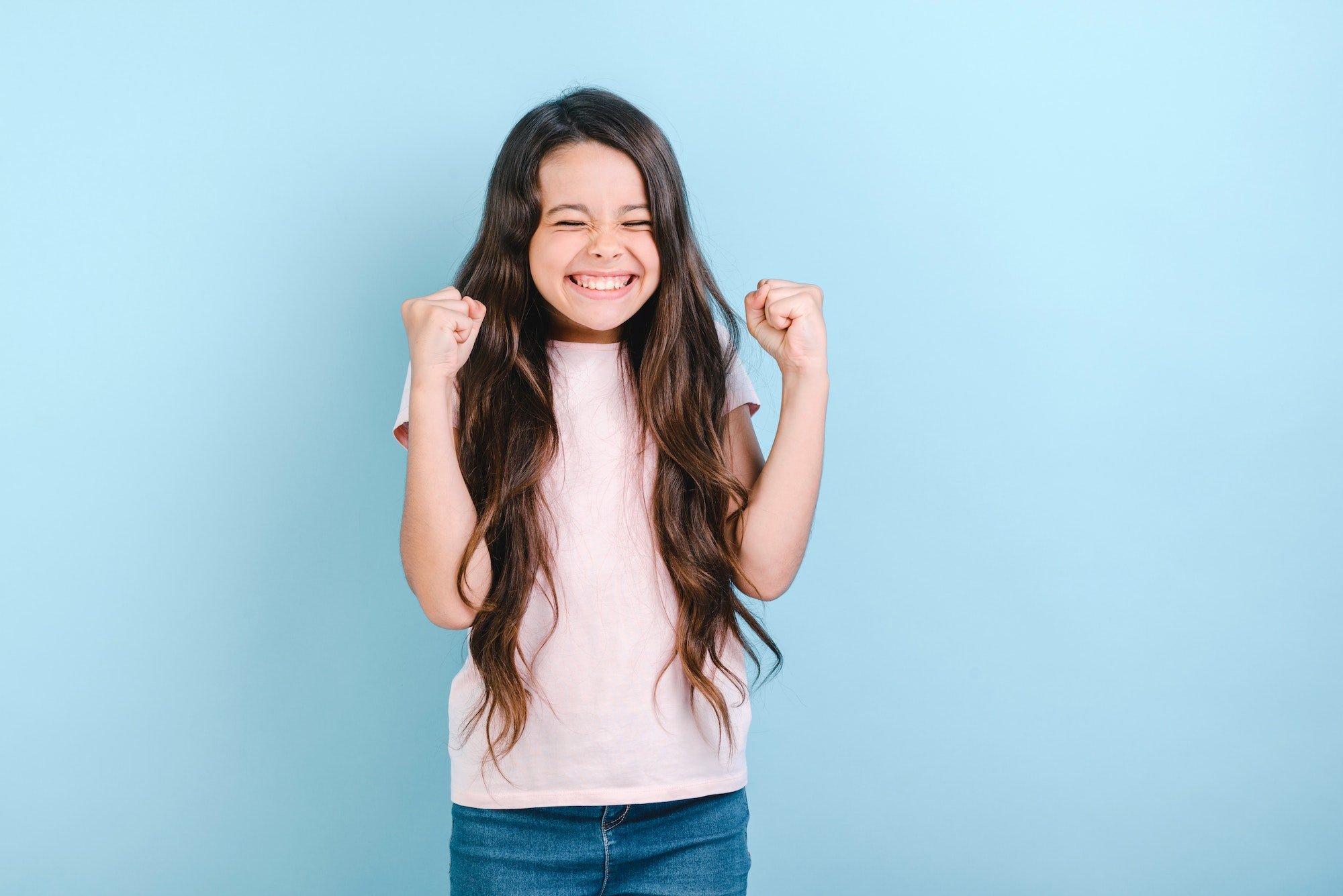 Happy child girl with closed eyes holds fists up in winner gesture- Image