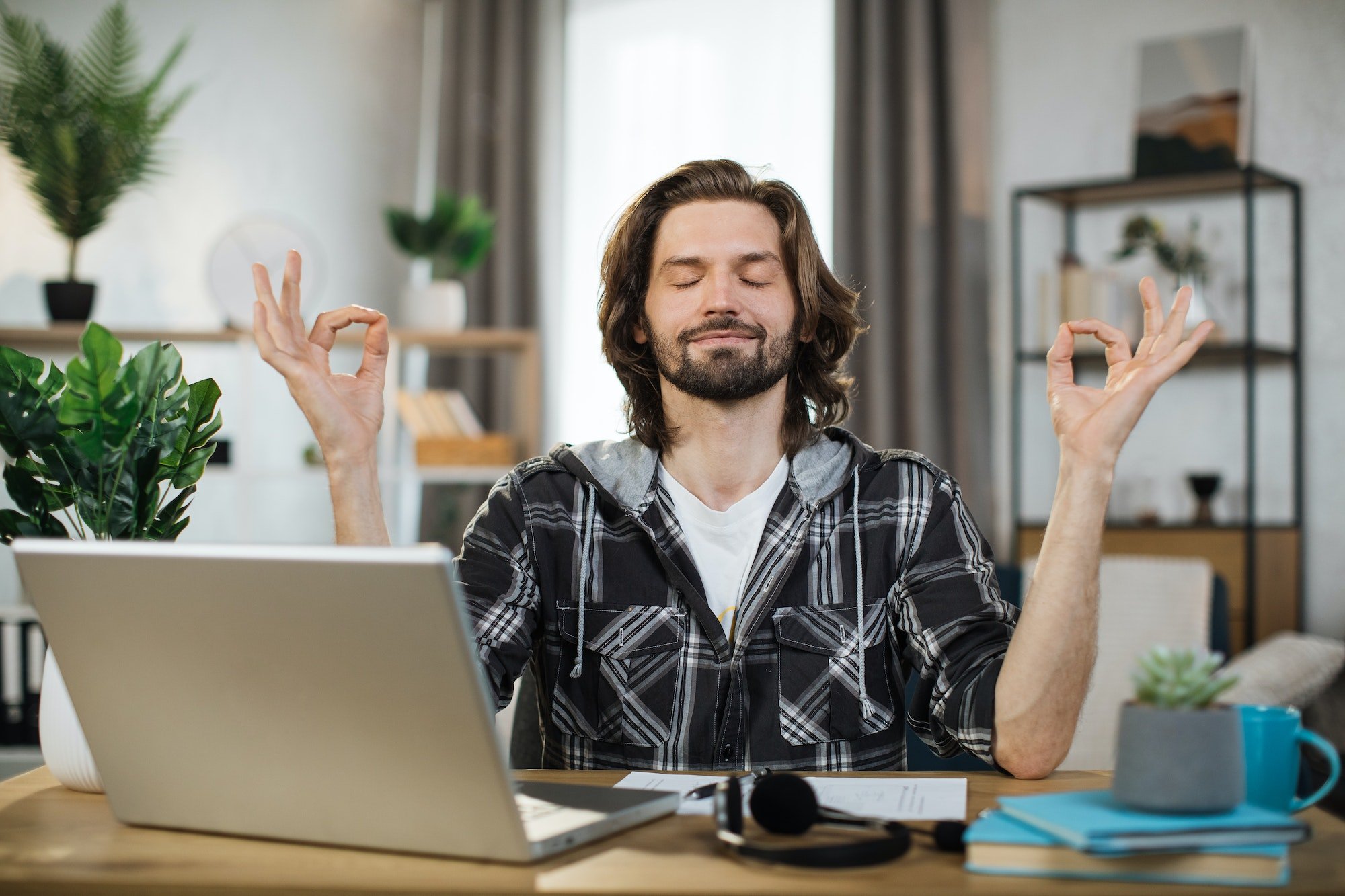 Man freelancer in eyeglasses sitting at table with closed eyes and relieving stress by meditation